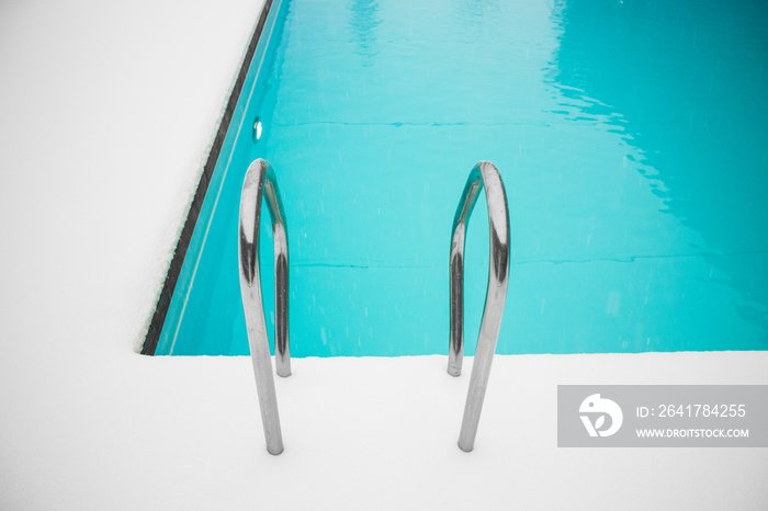 Beautiful blue color swimming pool in winter, poolside covered with white soft snow.