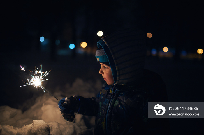 boy holds a sparkler in his hands while celebrating a new year on the street at night.