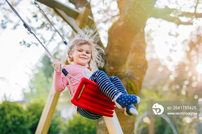 Happy beautiful little toddler girl having fun on swing in domestic garden. Cute healthy child swing