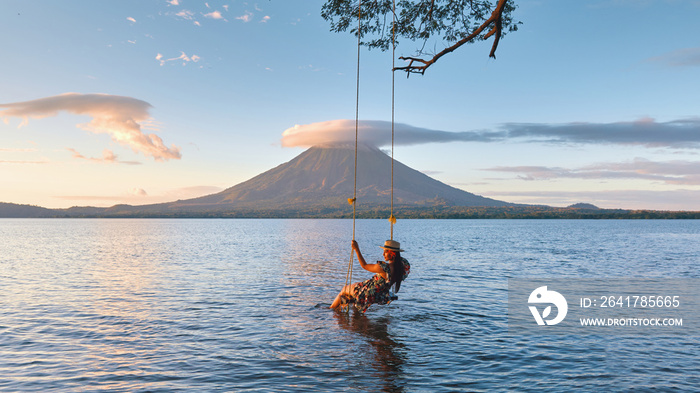 Woman sitting on swing in the lake with a beautiful view to the concepcion volcano during sunset in 