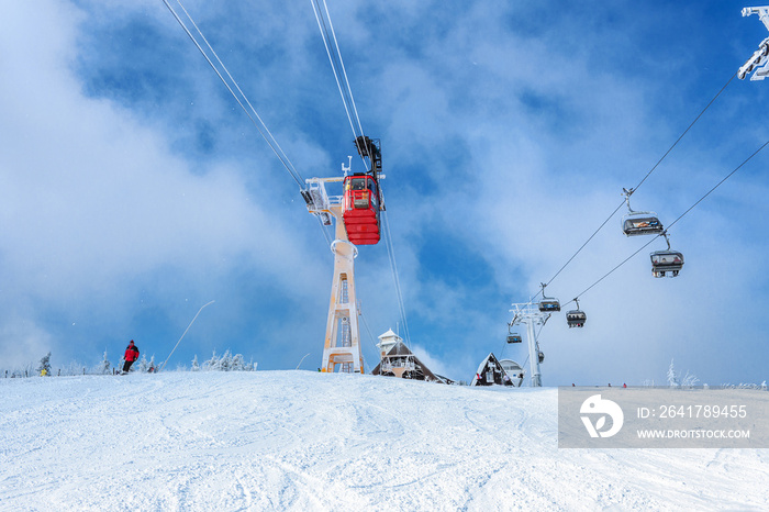 Seilbahn, Schwebebahn vor blaumem Himmel mit vereistem Mast, neben Sessellift, mit Berghütte im Hint