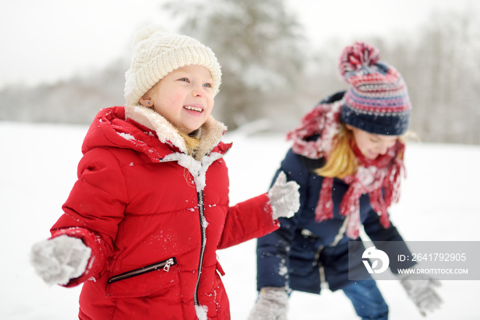 Two adorable little girls having fun together in beautiful winter park. Beautiful sisters playing in