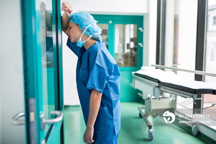 Sad surgeon leaning against the glass door