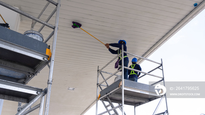 Low angle view of 2 cleaners on scaffolding using flat mops to cleaning white ceiling roof of petrol