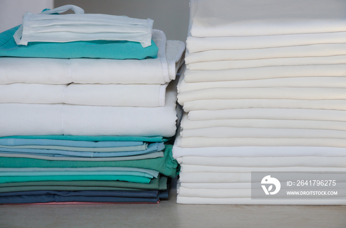 Stack of folded white linens and green surgery clothes in an industrial laundry.