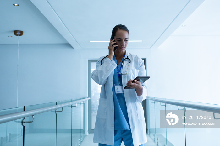 Female surgeon talking on mobile phone while using digital tablet at hospital