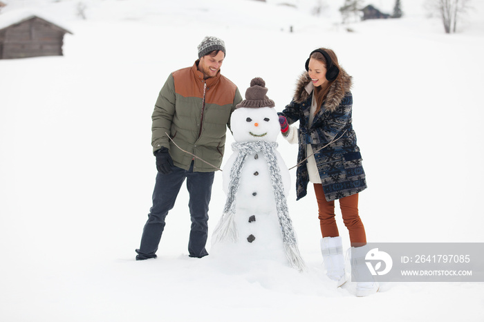 Happy young couple with snowman in snowy field