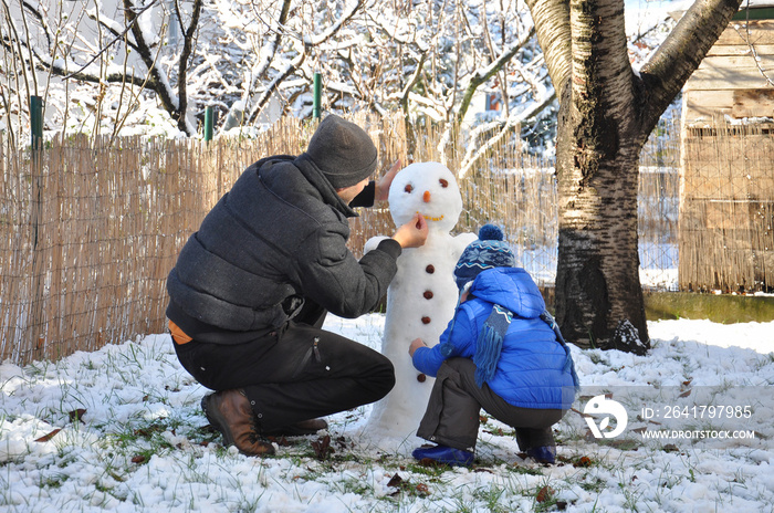 父亲和儿子在后院堆雪人。快乐的一家人在雪地上玩耍