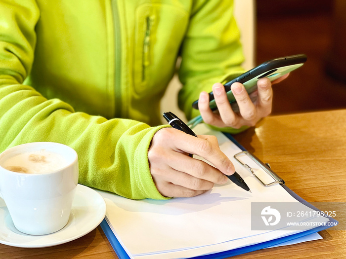 スマホを見ながら書類を書く手元と飲み物