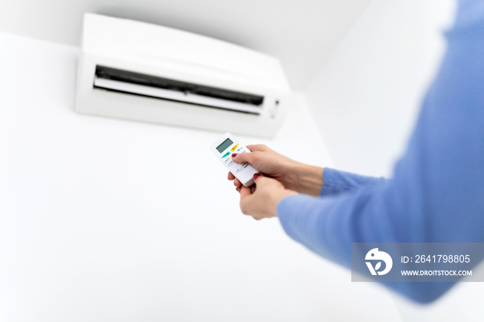 Woman holding a remote of a modern airconditioner unit at home.