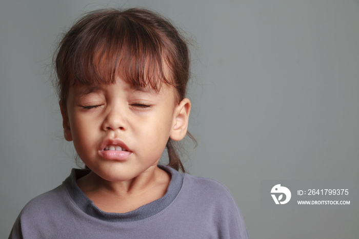 Girl child sneezing on a gray background.