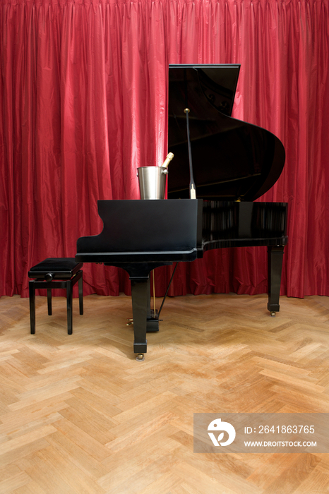 Grand Piano with a champagne cooler and bottle on a stage in front of a red curtain