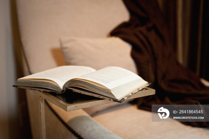 Upholstered armchair with shawl and book against wall at home