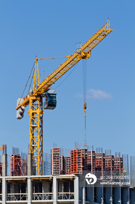 Yellow construction tower crane and house under construction