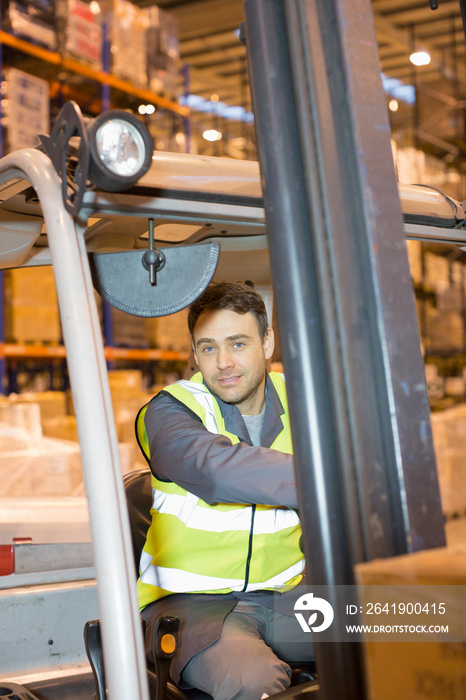 Portrait male worker driving forklift in distribution warehouse