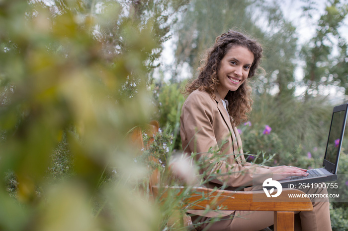 Portrait smiling businesswoman working at laptop on garden bench