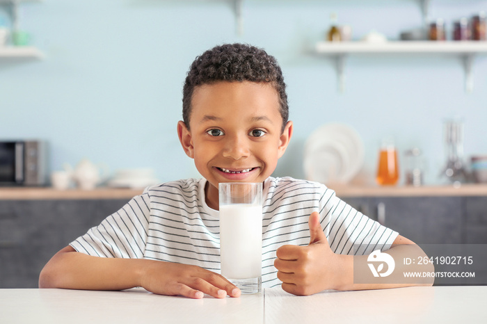 Cute African-American boy with glass of milk showing thumb-up at table