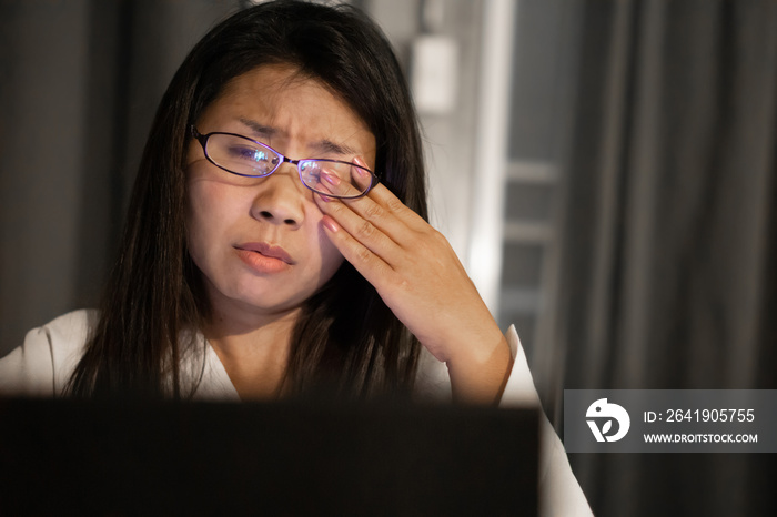 Asian woman suffering from eye strain tired from overwork on computer screen late at night