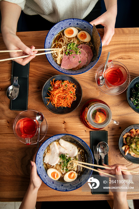 Top view on two people eat japanes ramen noodle soups and other asian dishes