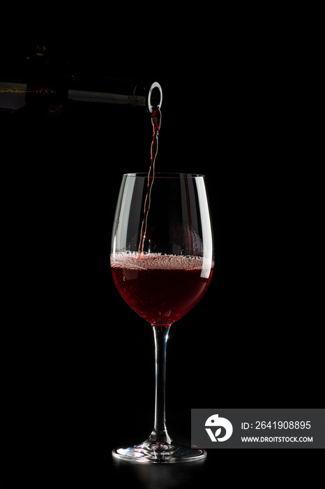 Red wine pouring into a glass with drops on black background