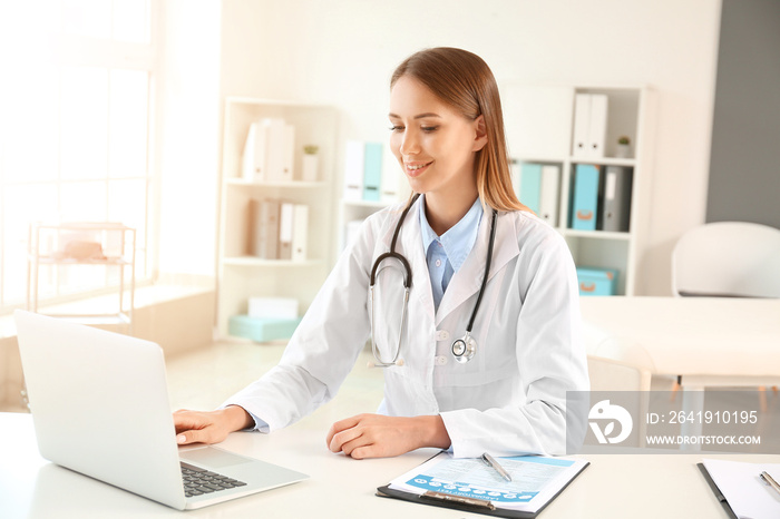 Female doctor working with laptop at table in clinic