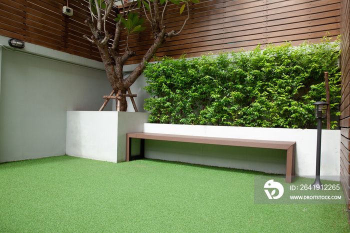 Modern backyard patio with green artificial grass, long wood bench, concrete and wood wall, modern l