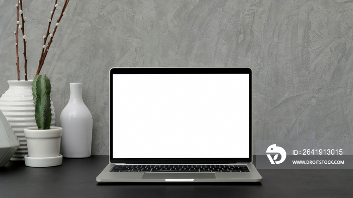Cropped shot of modern workspace with blank screen laptop and ceramic vase on black desk with grey l