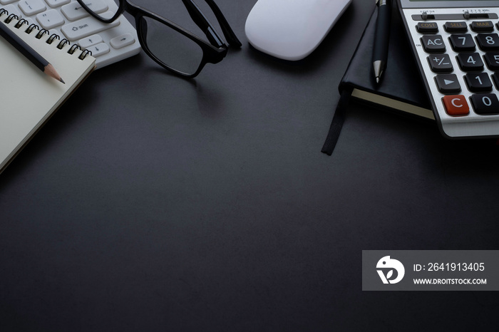 Workplace office with dark grey desk. Close-up view from above of keyboard, glasses with notebook an