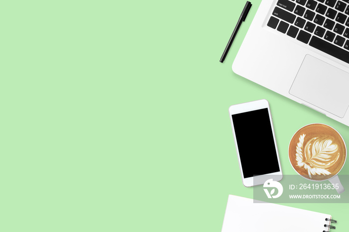 绿色粉彩办公桌，配有笔记本电脑、智能手机、拿铁咖啡和用品。俯视图
