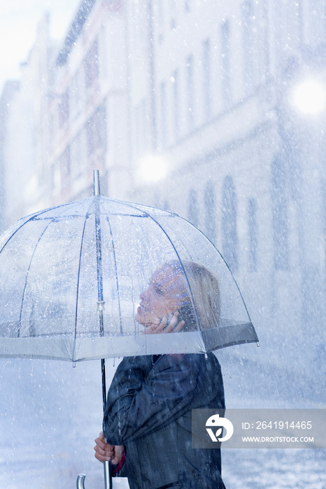 Businesswoman with umbrella talking on smart phone in rain