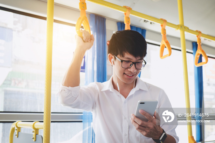 年轻的亚洲男子旅行者站在公交车上用智能手机听音乐，面带幸福的微笑，tr