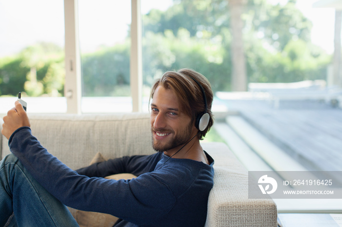 Portrait smiling young man listening to music with headphones on sofa