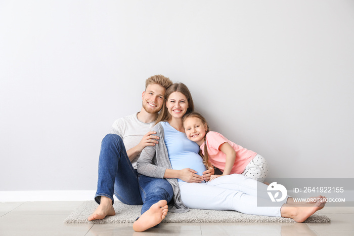 Beautiful pregnant woman with her family sitting near light wall