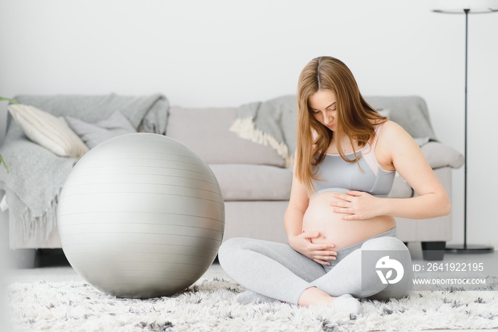Young pregnant woman exercising yoga with fit ball at home