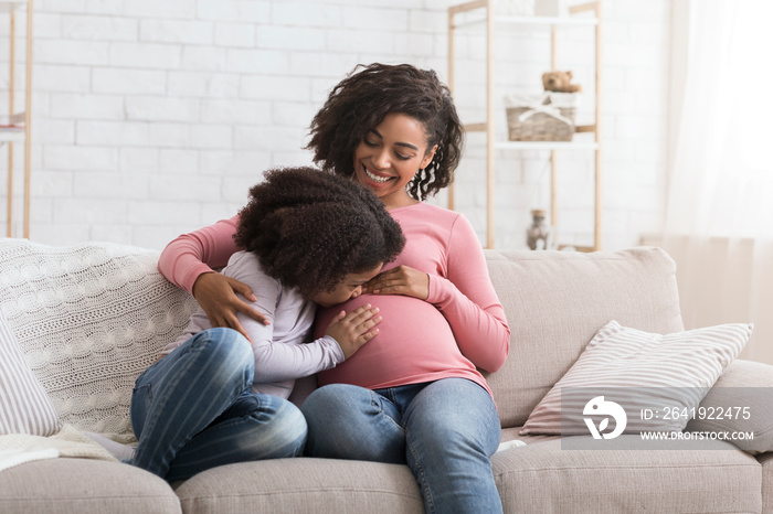 Adorable little african girl kissing and hugging her pregnant moms tummy