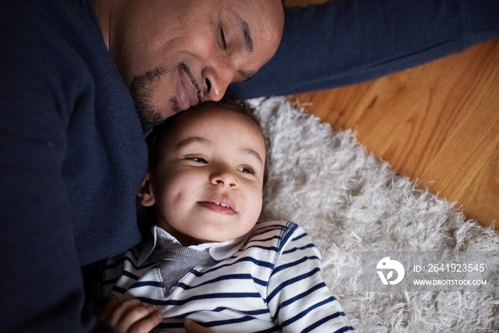 High angle view of loving father embracing cute son while sleeping on rug at home