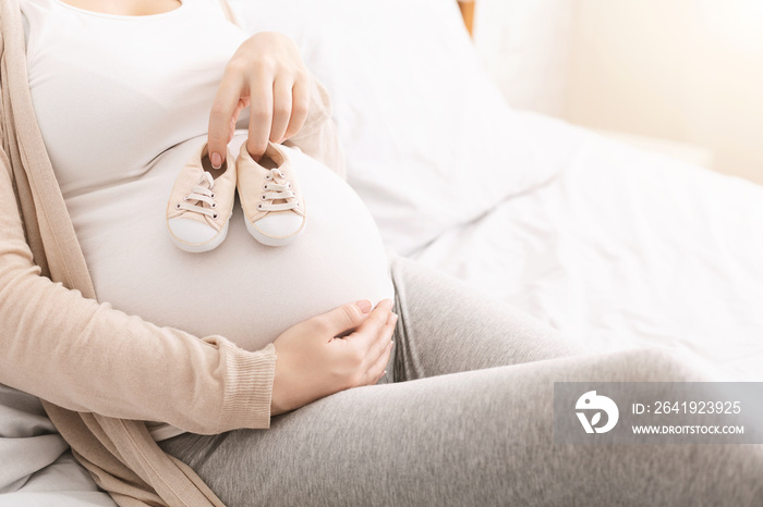 Small shoes for unborn baby on belly of pregnant woman