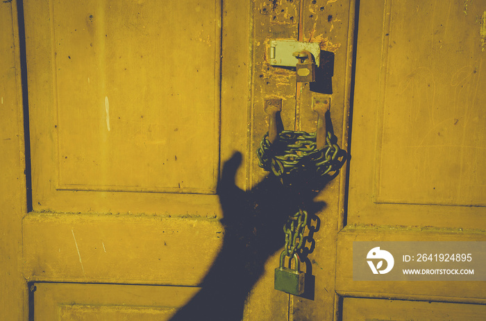 old wooden door locked with rusty chain and padlock and shadow man hand open the door. at night home