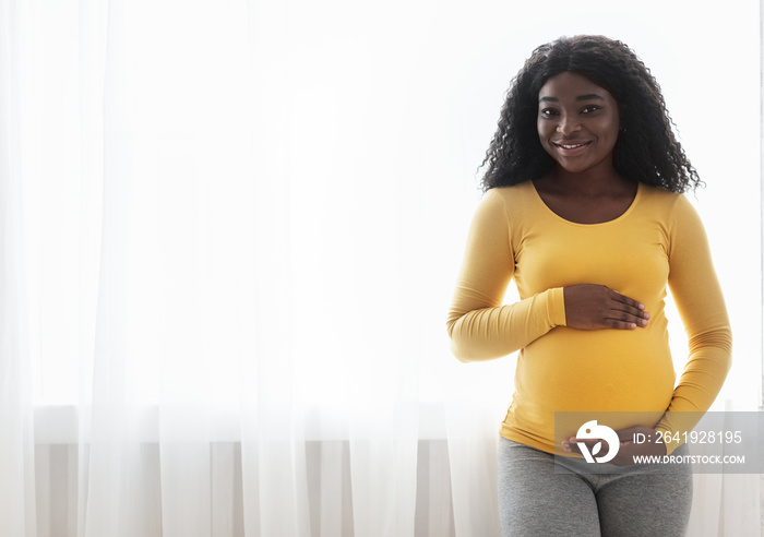 Smiling black lady carrying baby, hugging her big tummy