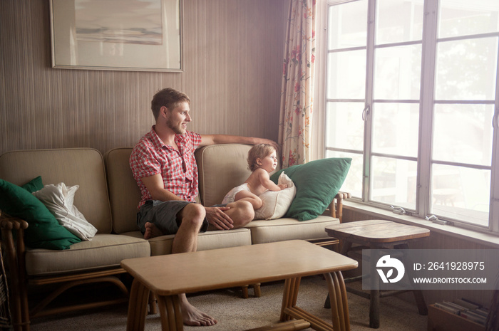 Father and baby (12-17 months) looking out window from couch