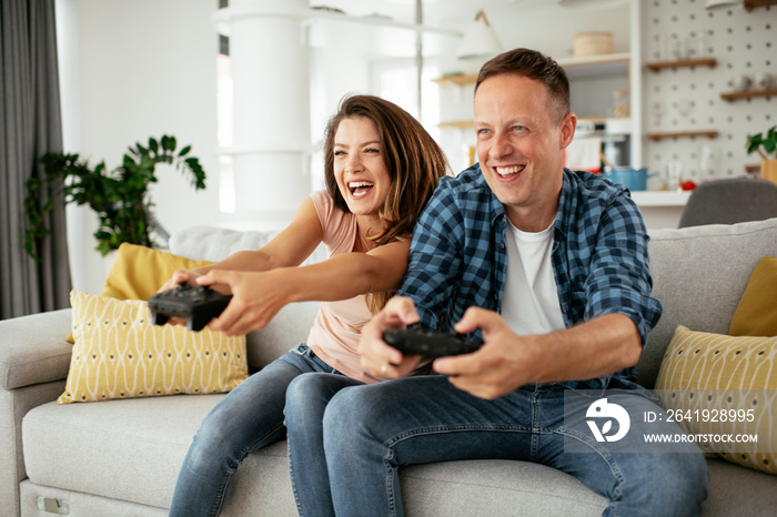 Husband and wife playing video game with joysticks in living room. Loving couple are playing video g