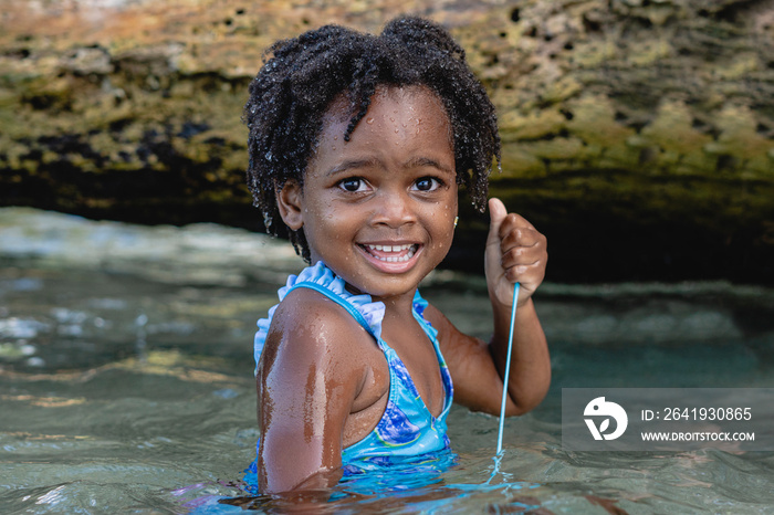 Imagen horizontal de una hermosa niña afroamericana de cabello afro muy sonriente en la playa jugand