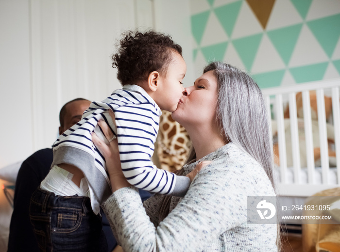 Mother kissing son while sitting with father against wall at home