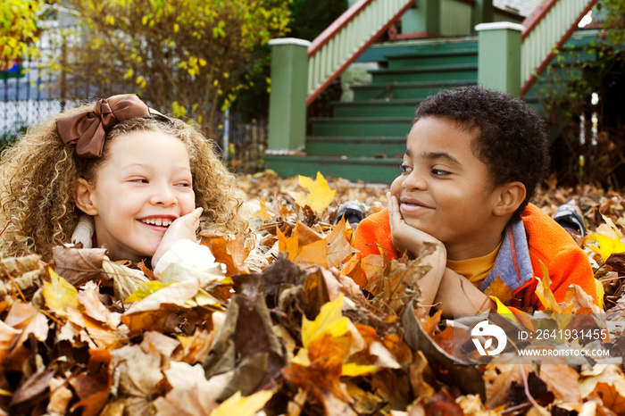 Cheerful friends looking at each other while lying on dried leaves during autumn