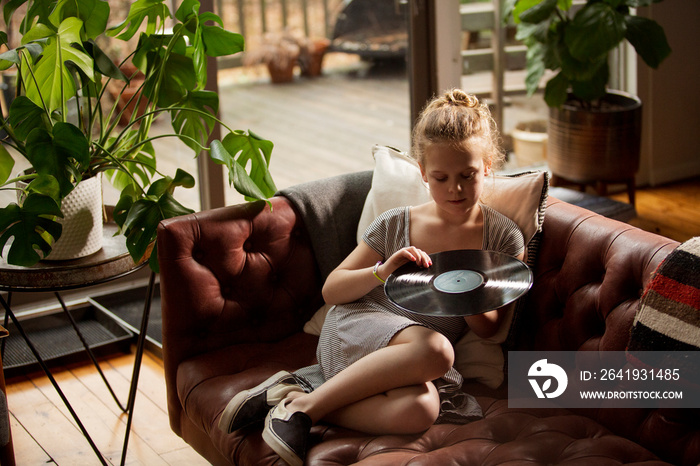 High angle view of girl holding turntable while relaxing on sofa at home