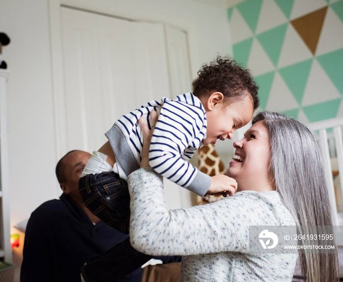 Happy mother picking up cute son while sitting with father against wall at home