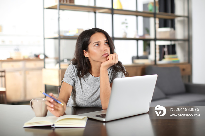 Thoughtful young woman working with laptop at home