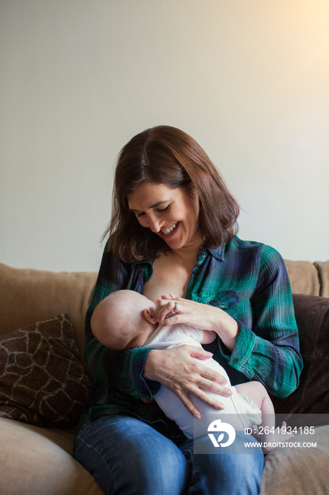 微笑的女人坐在家里的沙发上哺乳女儿