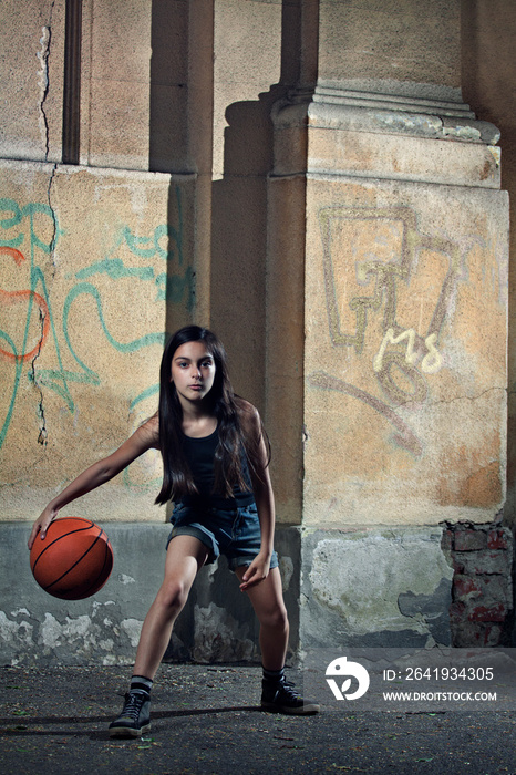 Portrait of girl playing basket ball against wall