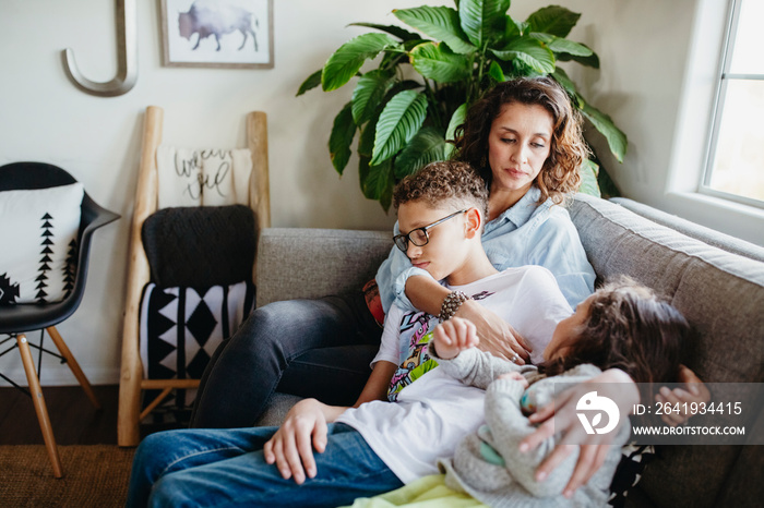 Mother with sleeping children sitting on sofa at home